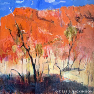 Orange rocky hills with a bright blue sky above and green yellow gum trees in the foreground