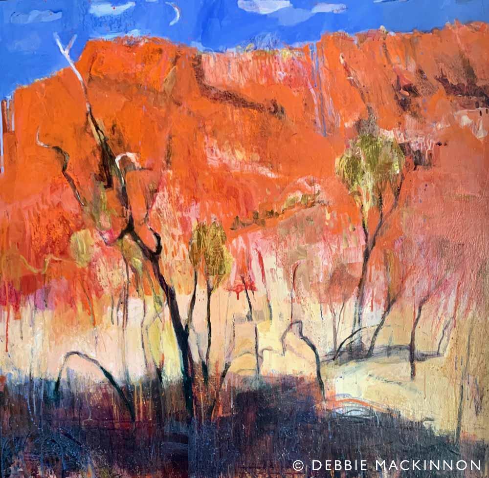 Orange rocky hills with a bright blue sky above and green yellow gum trees in the foreground