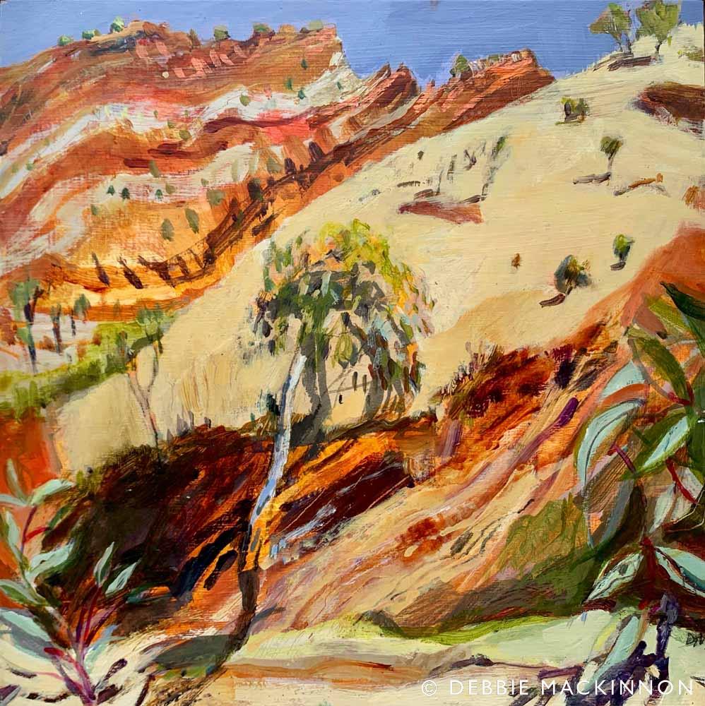 Orange rocky hills with yellow hills and green gum trees in the foreground