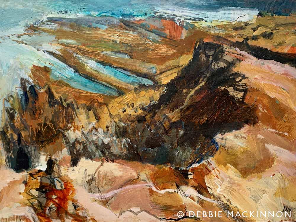Colourful orange and pink rocks with jagged edges reaching out into a turquoise sea